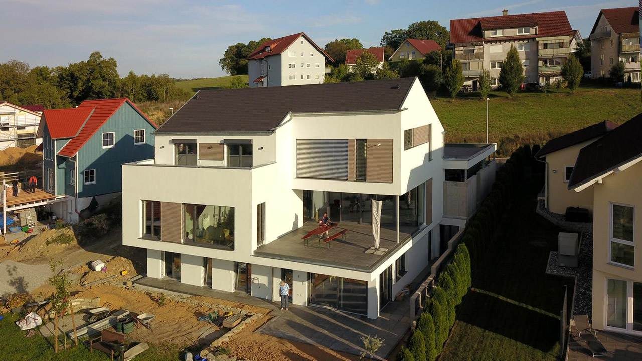 Außenaufnahme eines modernen Neubau-Einfamilienhaus mit weißer Fassade und Holzelementen zwischen den Fenstern und Terrassen.
