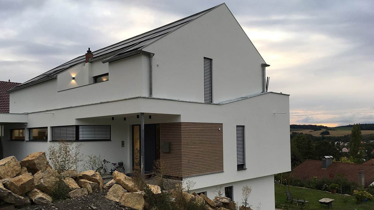 Außenaufnahmen eines modernen Neubau-Einfamilienhaus mit weißer Fassade und Holzelementen im Eingangsbereich.